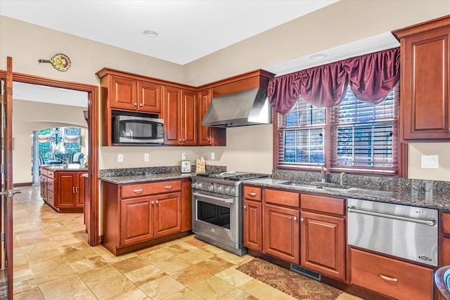 kitchen featuring dark stone counters, stainless steel appliances, sink, and wall chimney range hood