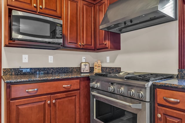 kitchen featuring wall chimney exhaust hood, appliances with stainless steel finishes, and dark stone countertops