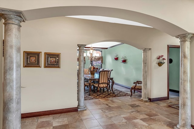 hallway featuring ornate columns and an inviting chandelier