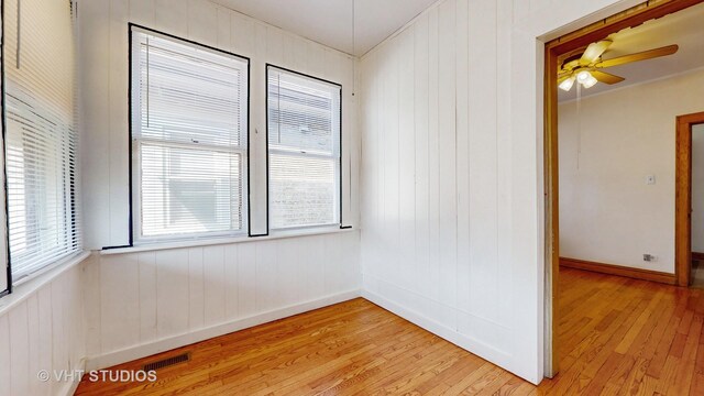 spare room featuring light wood-type flooring, ceiling fan, and wooden walls