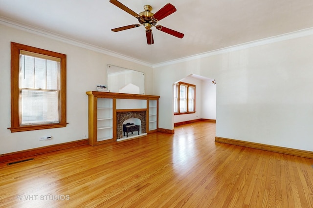 unfurnished living room with light wood-type flooring, ornamental molding, a brick fireplace, and ceiling fan