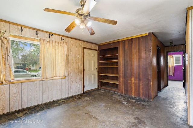 interior space with wood walls, concrete floors, and ceiling fan