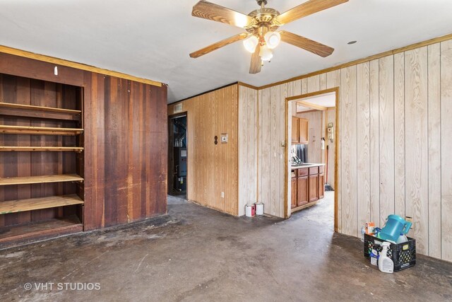 unfurnished bedroom with wooden walls, concrete flooring, crown molding, and ceiling fan