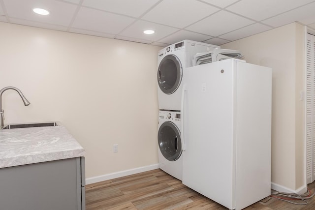 clothes washing area featuring light wood finished floors, stacked washer / drying machine, baseboards, and a sink