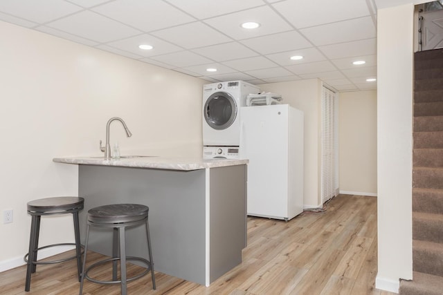 kitchen with a kitchen bar, a sink, freestanding refrigerator, light wood-style floors, and stacked washer / dryer