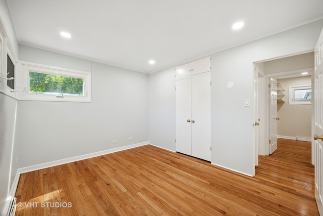 unfurnished bedroom with light wood-type flooring, a closet, and a baseboard heating unit