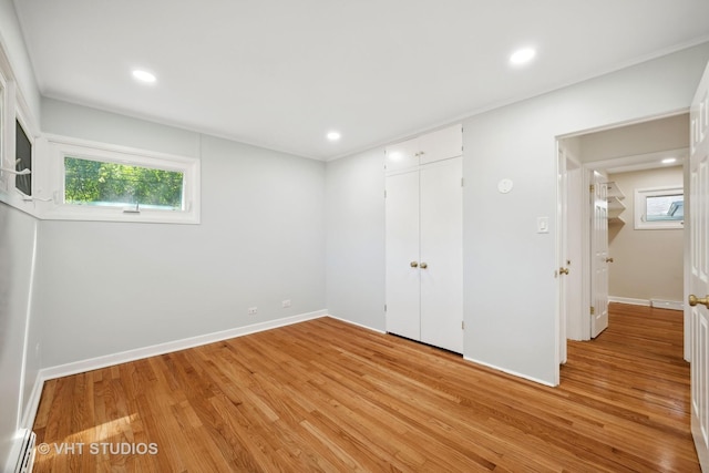 unfurnished bedroom featuring baseboards, multiple windows, a baseboard heating unit, and light wood-type flooring