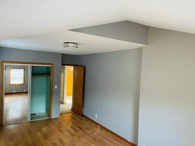 unfurnished bedroom featuring vaulted ceiling, wood-type flooring, and a closet