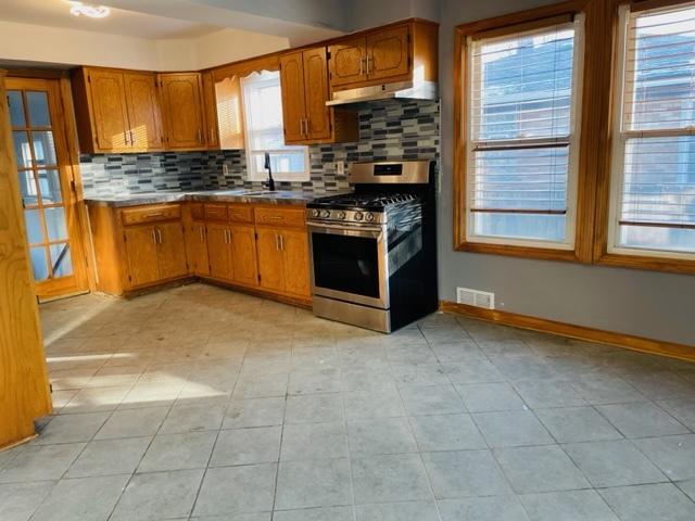 kitchen with gas stove, tasteful backsplash, light tile patterned flooring, and sink