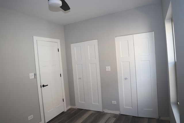 unfurnished bedroom featuring dark wood-type flooring, ceiling fan, and two closets