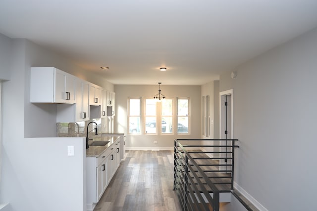 kitchen with light stone countertops, sink, white cabinetry, a notable chandelier, and dark hardwood / wood-style floors