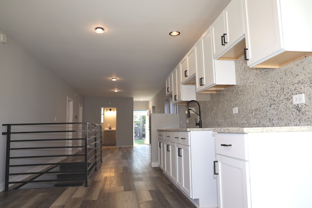 kitchen featuring tasteful backsplash, sink, white cabinetry, dark wood-type flooring, and light stone counters