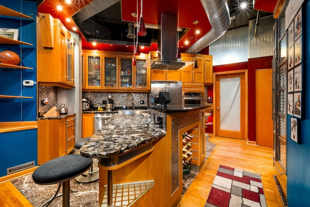 kitchen with sink, island range hood, light hardwood / wood-style flooring, backsplash, and appliances with stainless steel finishes