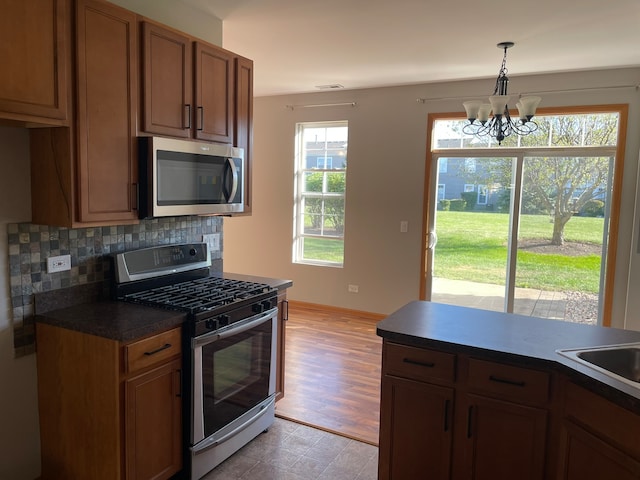 kitchen featuring a notable chandelier, light hardwood / wood-style flooring, backsplash, appliances with stainless steel finishes, and decorative light fixtures