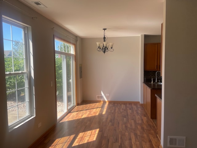 unfurnished dining area with an inviting chandelier, plenty of natural light, dark hardwood / wood-style floors, and sink