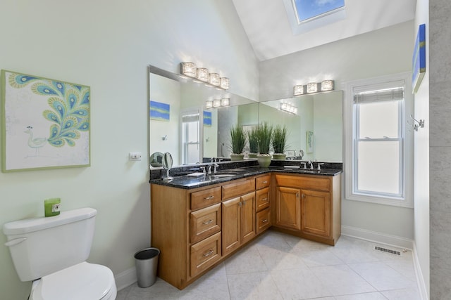 bathroom featuring tile patterned flooring, vanity, toilet, and vaulted ceiling with skylight