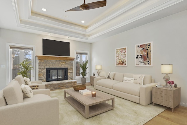 living room with a tray ceiling, ceiling fan, a fireplace, and light hardwood / wood-style flooring