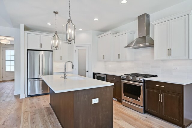 kitchen featuring sink, stainless steel appliances, wall chimney exhaust hood, and a center island with sink