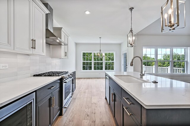 kitchen with wall chimney exhaust hood, stainless steel appliances, sink, a chandelier, and white cabinetry