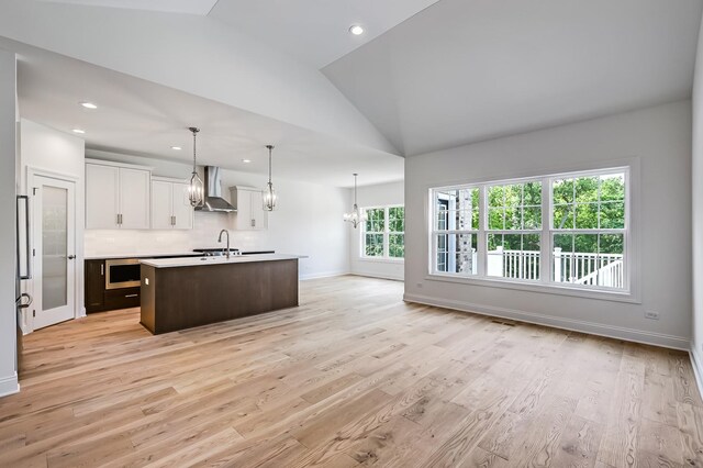 kitchen featuring light wood-type flooring, white cabinetry, an island with sink, wall chimney exhaust hood, and lofted ceiling