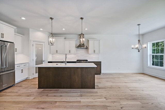 kitchen featuring light wood-type flooring, a kitchen island with sink, stainless steel appliances, sink, and wall chimney exhaust hood