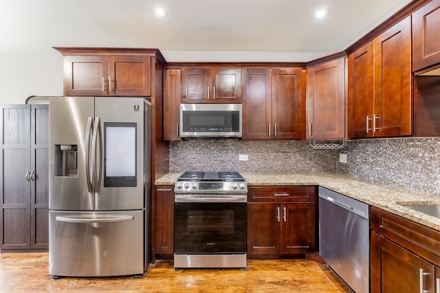 kitchen featuring light hardwood / wood-style flooring, stainless steel appliances, light stone countertops, and decorative backsplash