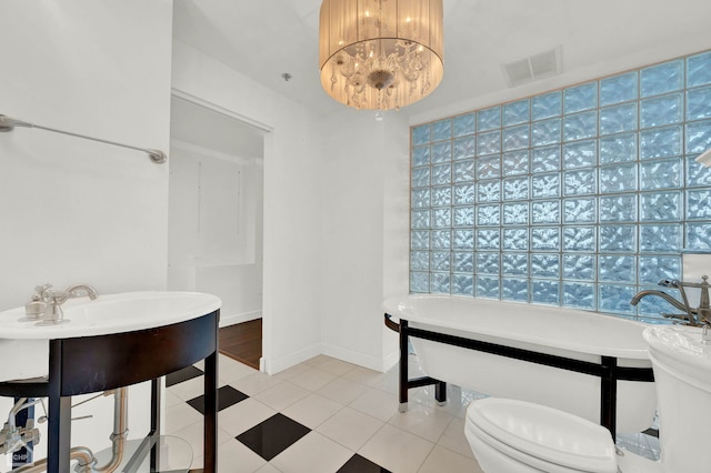 bathroom with a tub, toilet, a notable chandelier, and tile patterned floors