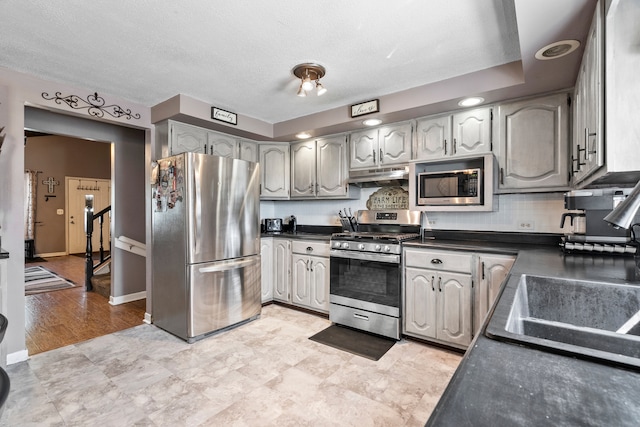 kitchen featuring under cabinet range hood, a sink, baseboards, appliances with stainless steel finishes, and dark countertops