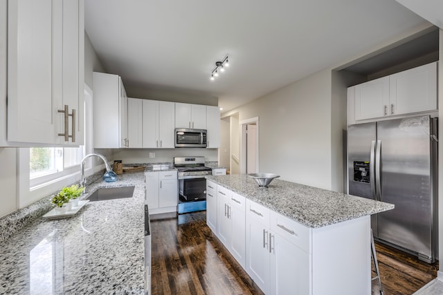 kitchen with appliances with stainless steel finishes, light stone counters, dark hardwood / wood-style flooring, sink, and a kitchen island