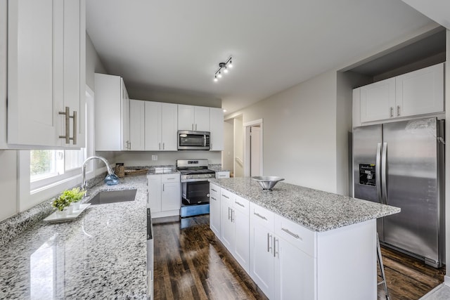 kitchen with stainless steel appliances, a kitchen island, a sink, light stone countertops, and dark wood-style floors