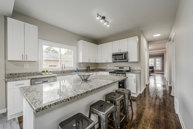 kitchen featuring appliances with stainless steel finishes, dark hardwood / wood-style flooring, white cabinetry, a breakfast bar area, and a kitchen island