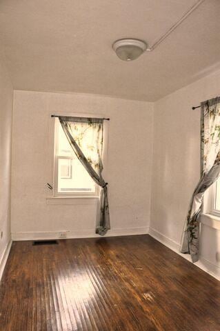spare room with baseboards and dark wood-type flooring