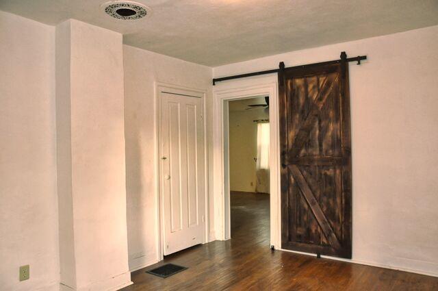 unfurnished room featuring a barn door, baseboards, visible vents, and dark wood-style floors