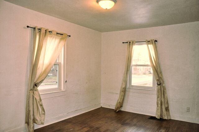 unfurnished room with baseboards, a healthy amount of sunlight, and dark wood-style floors