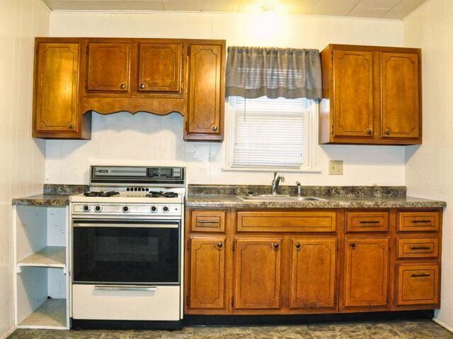 kitchen featuring ornamental molding, dark countertops, range with gas stovetop, and a sink