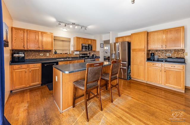 kitchen with light wood-type flooring, appliances with stainless steel finishes, a kitchen island, and a breakfast bar area