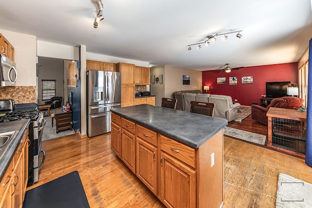 kitchen featuring light hardwood / wood-style floors, tasteful backsplash, a kitchen island, stainless steel appliances, and ceiling fan