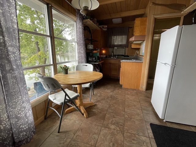 kitchen featuring extractor fan, dark tile patterned floors, sink, white fridge, and wood walls