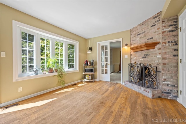 unfurnished living room with a wealth of natural light, light hardwood / wood-style floors, and a brick fireplace