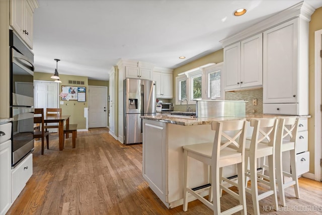 kitchen with pendant lighting, stainless steel appliances, a kitchen breakfast bar, light stone counters, and light hardwood / wood-style floors