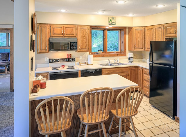 kitchen with a peninsula, a sink, black appliances, light countertops, and a kitchen bar