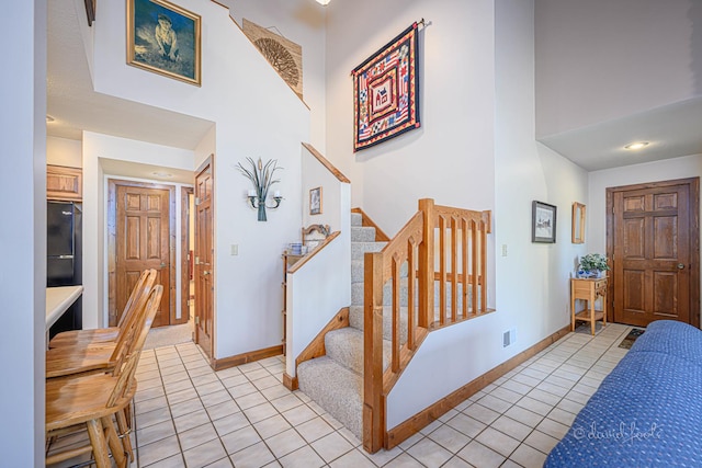 foyer entrance featuring stairs, a high ceiling, light tile patterned flooring, and baseboards