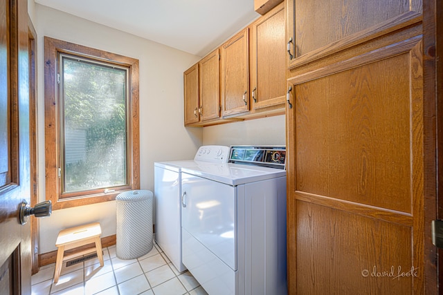 washroom with a wealth of natural light, washing machine and clothes dryer, cabinets, and light tile patterned flooring