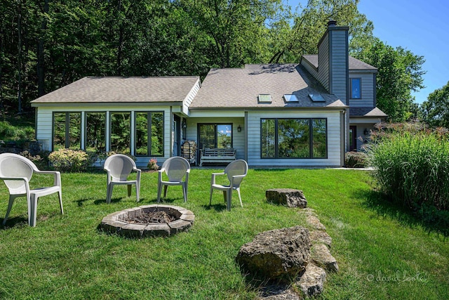 back of house featuring a yard, a chimney, roof with shingles, and an outdoor fire pit