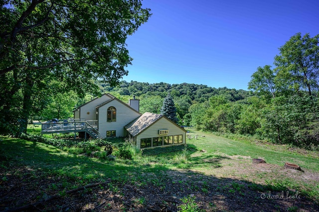 back of property with a wooden deck, a yard, a view of trees, and a chimney