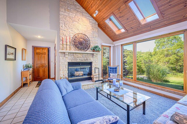 living room with high vaulted ceiling, tile patterned floors, a skylight, a stone fireplace, and wooden ceiling