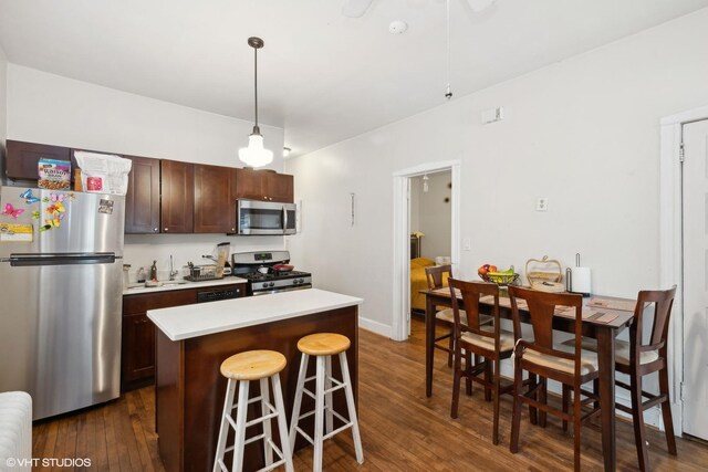 kitchen with a breakfast bar area, dark hardwood / wood-style floors, a center island, stainless steel appliances, and hanging light fixtures