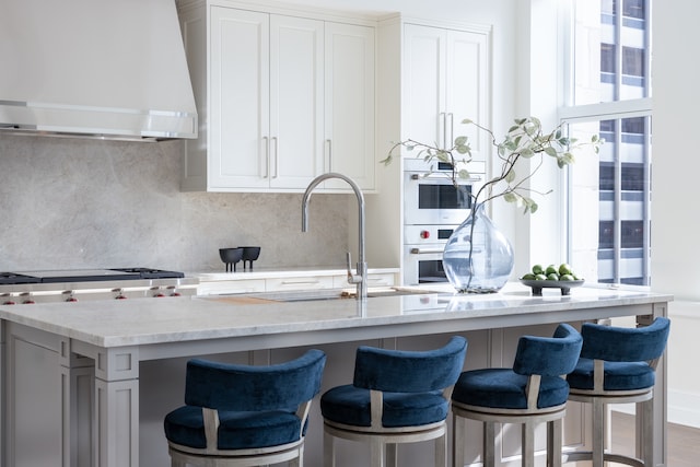 kitchen featuring light stone countertops, plenty of natural light, decorative backsplash, and range hood