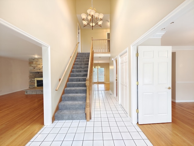 stairway with hardwood / wood-style flooring, crown molding, a chandelier, a stone fireplace, and a towering ceiling