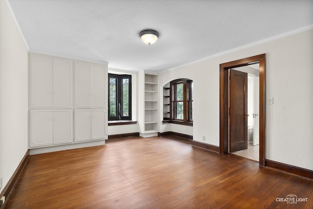 unfurnished room featuring built in shelves, dark hardwood / wood-style floors, and ornamental molding